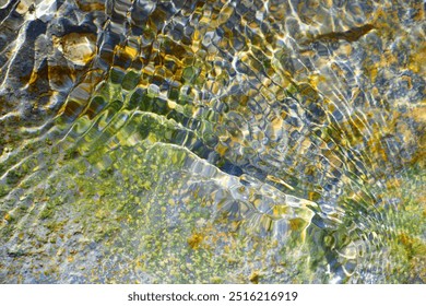 Reflection the Sun rays on the rocks under the water flow at the river