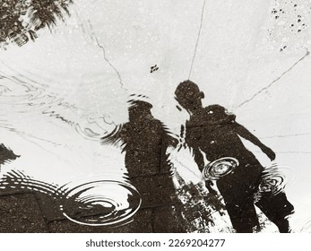Reflection of two children playing in a puddle of rain