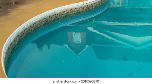 reflection of urban house in blue water of backyard pool with a curved round edge and vinyl sides reflection includes rooftop of red brick house windows triangular peaks upside down in water