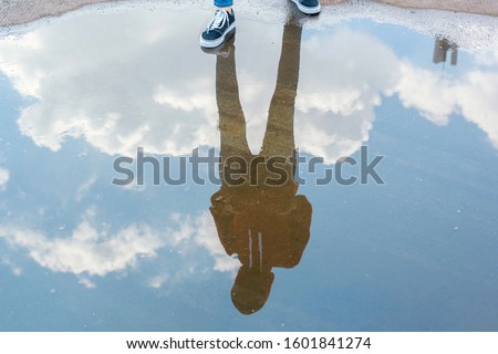 Reflection in water of man with casual style standing in bright blue sky 