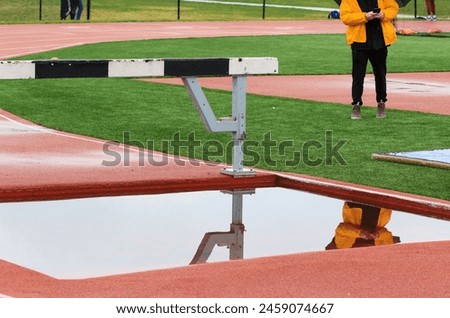Reflection in the water of a track steeplechase water pit on a calm day.
