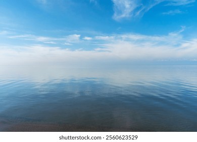 Reflection of white clouds in Issyk Kul Lake during very calm weather with almost no wind. Blue is intermixed with white above and below. Beautiful nature scenery in Kyrgyzstan.