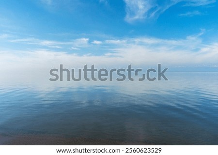 Reflection of white clouds in Issyk Kul Lake during very calm weather with almost no wind. Blue is intermixed with white above and below. Beautiful nature scenery in Kyrgyzstan.