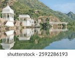 Reflection of white temple structures along lake Badi, an artificial fresh water lake near Udaipur, Rajasthan, India. Lush green mountains in the background