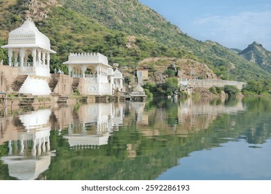 Reflection of white temple structures along lake Badi, an artificial fresh water lake near Udaipur, Rajasthan, India. Lush green mountains in the background