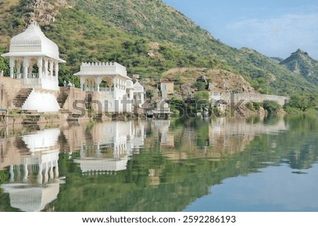 Reflection of white temple structures along lake Badi, an artificial fresh water lake near Udaipur, Rajasthan, India. Lush green mountains in the background