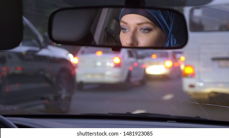 reflection of a woman in a hijab in a rearview mirror of a car while driving in a traffic jam in the evening. Muslim woman driving a car.