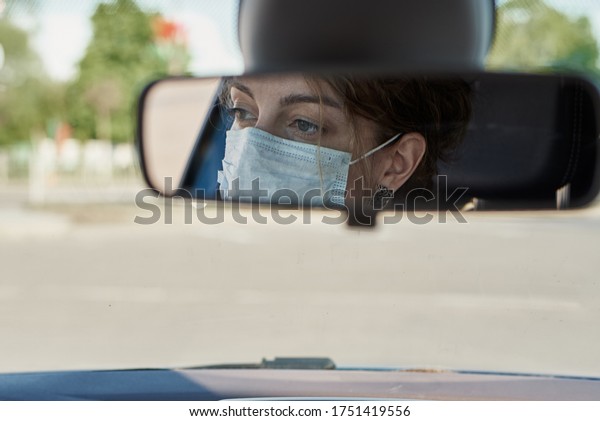 reflection of\
woman in protective medical mask in the rear view mirror in car.\
Virus protection and healt care\
concept