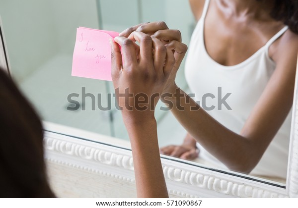 Reflection of woman sticking I love you word\
sticky note on\
mirror