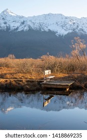 Reflection Of Wooden Chair On Lake In Glenorchy Lagoon With Willow Trees With Snow Mountains Background.