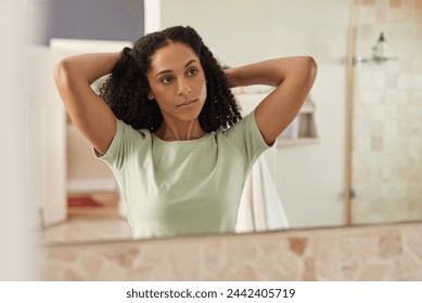 Reflection of a young African woman tying her long curly hair back in a mirror in her bathroom at home in the morning - Powered by Shutterstock