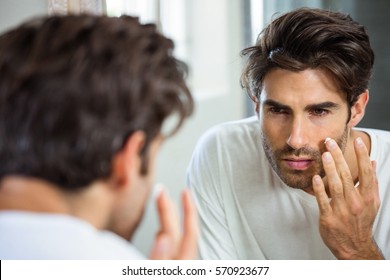 Reflection Of Young Man In Bathroom Mirror Applying Moisturizer On His Face