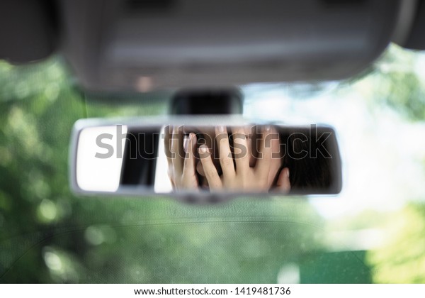 Reflection of young woman with\
frightened eyes covering her face with  hands in the car rear view\
mirror. Concept of an accident on the road or knock down\
pedestrian