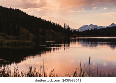 Reflections of clouds at sunset at Black Lake near Vail, Colorado with Rocky Mountain peaks visible behind a coniferous forest - Powered by Shutterstock