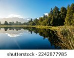 Reflections in Lake Mathieson surrounded by natural bush and forest and Southern Alps mountain range in South Island New Zealand.