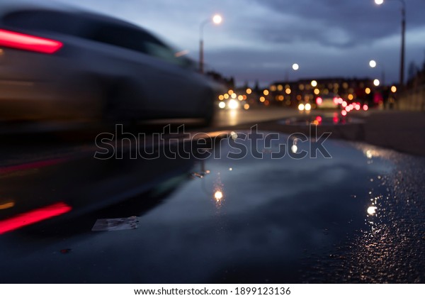reflections of lights in a puddle\
in the center of prague after rain in the background blurred\
cars