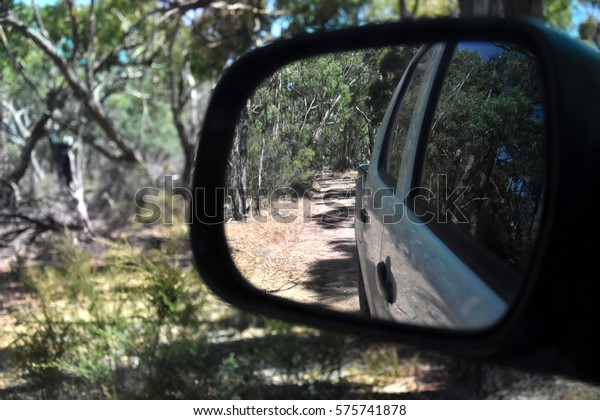 Reflections in a side view mirror of a car\
driving in the bush. Rear view car mirror in forest live green.\
Dirt road leading up to a slavery plantation. Concept of 4wd\
off-road driving in the\
nature.
