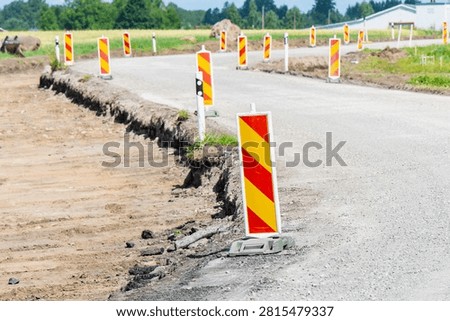 Reflective hazard marker posts delineating a road reconstruction zone with scraped dirt subgrade for traffic safety management