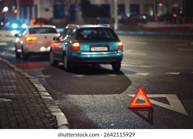 Reflective red warning triangle placed on dark road at night after rear-end collision between two vehicles to alert traffic and ensure safety in emergency conditions. Traffic hazard scene at night 