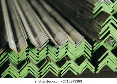 Reflective stack of stainless steel angle profiles. The shiny surface reflects the ambient warehouse environment, creating a dynamic look. The image conveys cleanliness and modernity, suitable for architectural applications where the metal might be exposed. It serves as a visual metaphor for 'modern industry' and 'high-tech construction'.