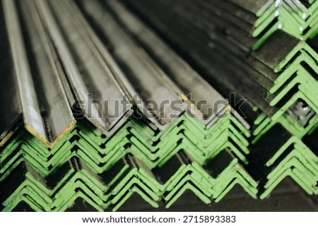 Reflective stack of stainless steel angle profiles. The shiny surface reflects the ambient warehouse environment, creating a dynamic look. The image conveys cleanliness and modernity, suitable for architectural applications where the metal might be exposed. It serves as a visual metaphor for 'modern industry' and 'high-tech construction'.