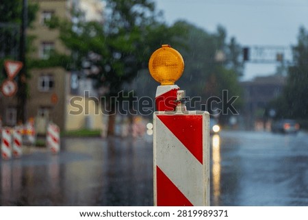 Reflective traffic delineator panel with yellow flashing light managing urban lane closure and roadwork safety during heavy rain