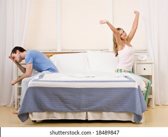 Refreshed Woman Waking Up Next To Tired Man