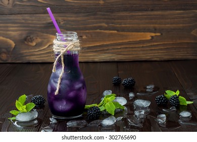 Refreshing blackberry juice in vintage eco style bottle on rustic dark wooden table. Cold summer berry drink with ice and mint. Copy space background. Clean eating