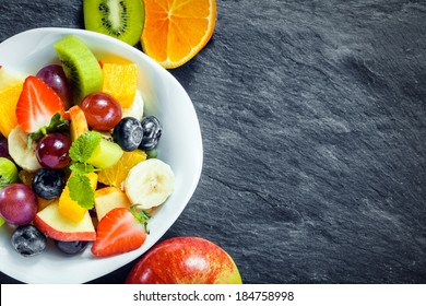 Refreshing Bowl Of Fresh Tropical Fruit Salad With Ingredients On A Textured Slate Kitchen Counter With Copyspace, Overhead View