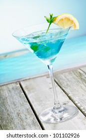 Refreshing classical blue curacao martini cocktail garnished with fresh lemon and served alongside the ocean on a tropical vacation