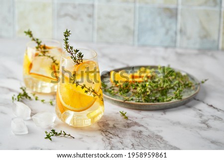 Refreshing cocktail with ice, orange and thyme. Refreshing summer homemade alcoholic or non-alcoholic cocktail or mocktail, or Detox infused flavored water.