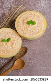 Refreshing Coco Melon Dessert Recipe With Tapioca Served In Melon Shells On Top Of A Table With Wooden Spoons