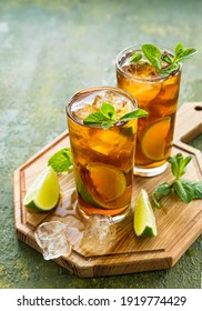 Refreshing Drink, Iced Tea With Lime Wedges In Glasses On A Wooden Board On A Green Concrete Background. Summer Drinks. Soft Drinks 