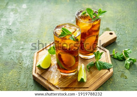 Refreshing drink, iced tea with lime wedges in glasses on a wooden board on a green concrete background. Summer drinks. Soft drinks 