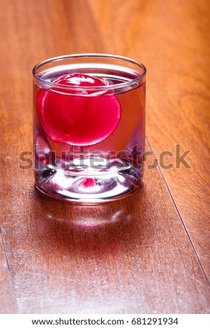 refreshing drink with a red ice ball releasing flavor into the cocktail as it melts and chills the beverage