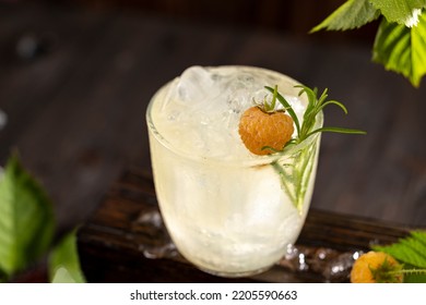 Refreshing drink of yellow raspberry surrounded raw ripe berries and green leaves. Dark wooden background. Backlight. Ready for drinking