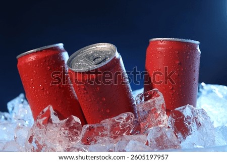 Refreshing drinks in cans on ice cubes against dark blue background, closeup