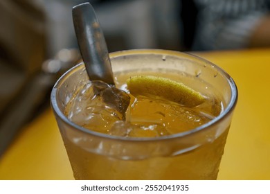 A refreshing glass of iced lemon tea with a lemon wedge, garnished with a sprig of mint, served with a spoon - Powered by Shutterstock