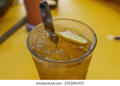 A refreshing glass of iced lemon tea with a lemon wedge, garnished with a sprig of mint, served with a spoon - Powered by Shutterstock