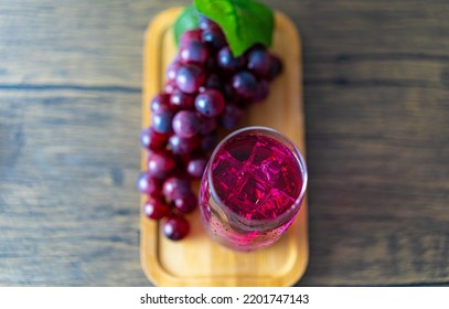 Refreshing A Glass Of Purple Grape Juice With Ice Cubes On Wooden Tray