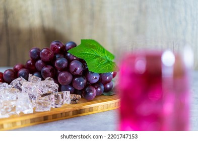 Refreshing A Glass Of Purple Grape Juice With Ice Cubes On Wooden Tray