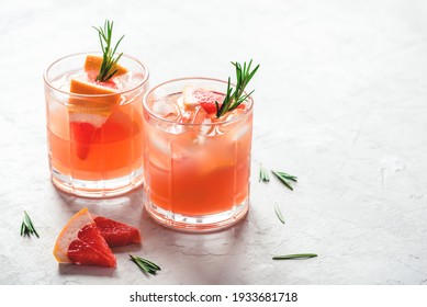 Refreshing grapefruit cocktail with ice and rosemary on a grey background.