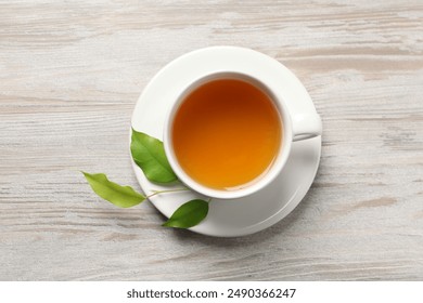 Refreshing green tea in cup and leaves on light wooden table, top view