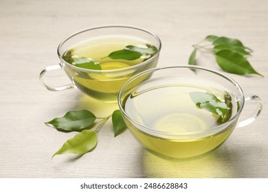 Refreshing green tea in cups and leaves on wooden table, closeup