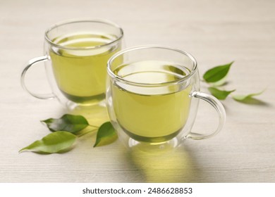 Refreshing green tea in cups and leaves on wooden table, closeup