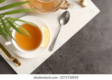 Refreshing green tea, spoon and slice of lemon served on dark textured table, top view. Space for text