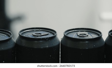 Refreshing and ice cold, unopened black aluminum cans are lined up, covered with condensation droplets, creating a visually appealing display of chilled beverages