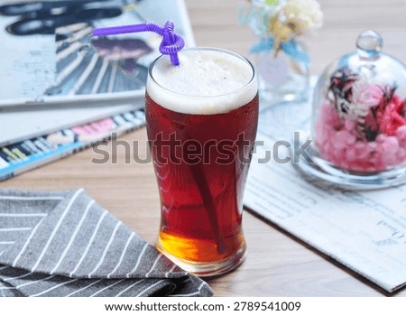 Refreshing iced bubble tea in clear glass with colorful straw, served on wooden table with pastel flowers in background.