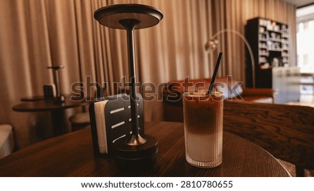A refreshing iced coffee with distinct layers of milk and espresso sits on a wooden table next to a modern lamp and a napkin holder