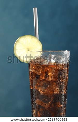 Refreshing iced cola with lime slice on blue background, closeup